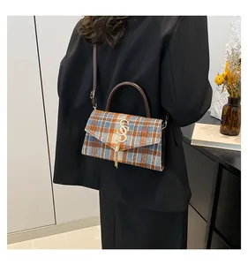 Detalle de bolso de cuadros con logotipo dorado y flecos, combinado con un blazer negro