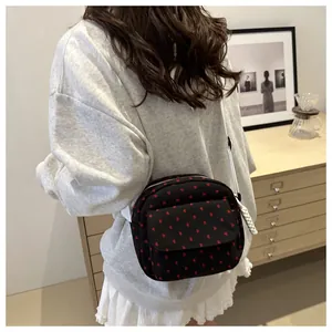 Detail of a black quilted crossbody bag with red hearts and a white woven shoulder strap