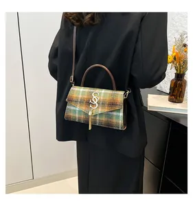 Detalle de un bolso bandolera de cuadros verdes con logo S metálico y borla elegante