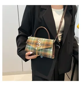 Detalle de bolso bandolera de lana a cuadros verde con cierre dorado y borla fina