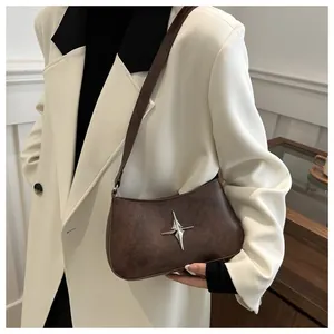 Gros plan d'un sac demi-lune marron foncé avec emblème étoile argentée sur un blazer blanc