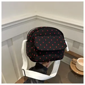 Close-up of a black crossbody bag with red heart patterns and white fabric strap