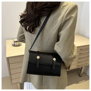 Detailweergave van een zwarte crossbodytas met goudkleurige gespen gedragen door een model