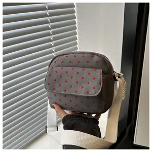 Close-up of grey canvas crossbody bag featuring red heart patterns and white strap