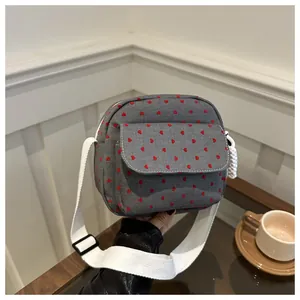 Detail of grey canvas crossbody bag with red heart embroidery and white woven strap