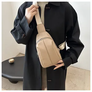 Detail of light khaki crossbody chest bag with wide strap on a black winter coat