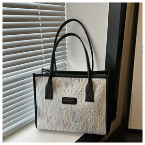 Detail of canvas tote bag showing black trim, leather straps and colorful wavy embroidery