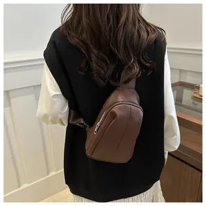 Detail of a brown leather cross-body chest bag with silver metal zipper and woven strap