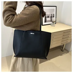Détail d'un grand sac cabas en cuir noir avec plaque métallique et longues anses d'épaule