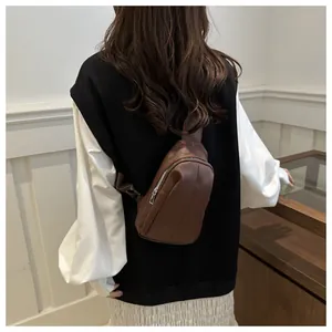 Detail view of dark brown leather crossbody chest bag with silver metal zipper on model