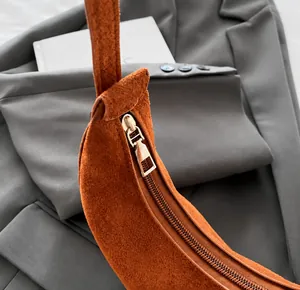 Detail view of smooth metal zipper and textured brown suede leather crescent bag