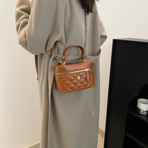 Borsa a secchiello trapuntata marrone con ciondolo a fiore dorato e tracolla su cappotto beige