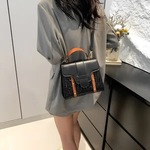 Minimalist black tote bag with orange handle shown from behind on a female model