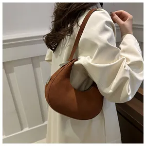 Close-up of brown suede crescent bag with silver buckle worn with a beige coat