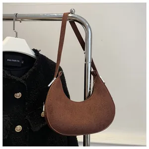 Detailed macro of brown suede crescent hobo bag hanging on a hanger with tweed coat