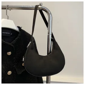 Detail of black suede crescent shoulder bag hanging against a minimalist interior wall