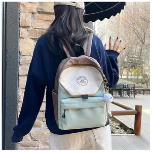 Mochila escolar tricolor marrón beige y verde con pompón blanco en un entorno exterior