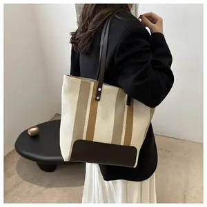 Dettaglio borsa tote tessuta a righe beige e marroni con manico in pelle e rivetto metallico