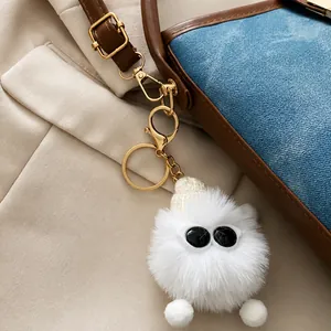 Detail of white fluffy pom-pom charm with sunglasses on a blue denim bucket bag