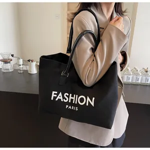 Detalle del bolso tote negro con letras blancas y asas de cuero llevado por modelo