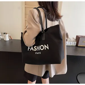 Detalle de un bolso tote grande de lona negra con letras blancas de Fashion Paris