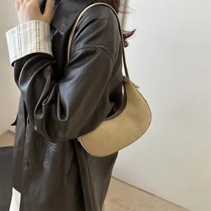 Minimalist light khaki suede hobo crescent bag worn over the shoulder on a leather coat