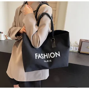 Detalle de bolso tote de lona negra con letras de fashion paris y asas de cuero