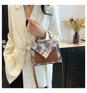 Detail of snake print faux leather handbag featuring a white clover clasp and brown strap