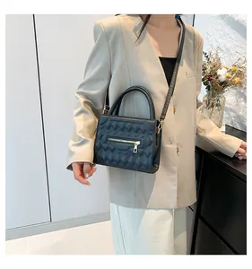 Dettaglio della borsa squadrata trapuntata nera con zip abbinata a un completo beige