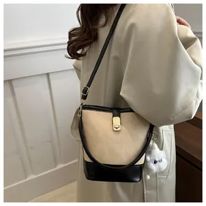 Vista detallada del bolso tipo cubo con cierre metálico y colgante de peluche en gabardina