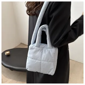 Primo piano di una borsa tote trapuntata celeste tenuta da una modella in cappotto nero