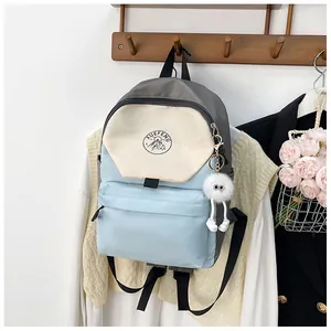 Primer plano de la mochila de lona bicolor con logo XUEFENG y colgante de bola de felpa