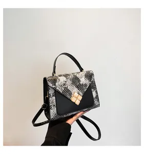 Detail of snakeskin print leather handbag with floral gemstone buckle and black top handle
