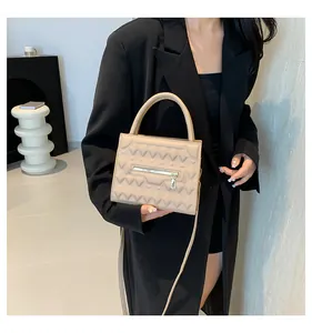 Dettaglio della borsa beige testurizzata su modella con giacca blazer nera