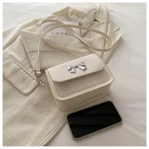 Detail view of cream flap square bag with silver bow buckle on elegant fabric background
