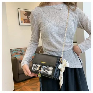 Detail of plaid leather crossbody bag with gold chain and white silk bow accessory