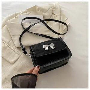 Detail of black crossbody bag featuring silver metal butterfly bow and suede texture