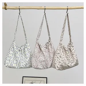 Détail de trois sacs cabas en toile à fleurs suspendus à une tringle en bois naturel