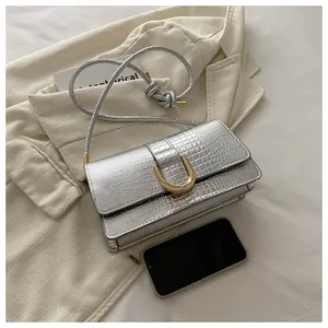 Sac à main argenté à motif crocodile avec boucle dorée et smartphone pour comparer la taille