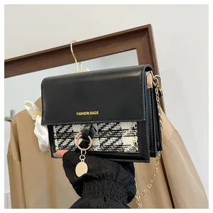 Detail of black leather and plaid tweed bag with gold chain and white silk bow accent