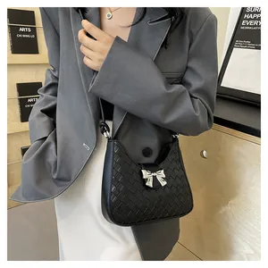 Detail showing black woven leather texture and silver metal bow on shoulder bag