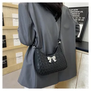 Detail of black woven shoulder bag featuring a silver metal bow clasp and sleek leather texture