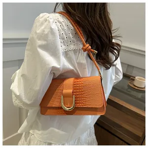Détail du sac à bandoulière orange en similicuir croco avec boucle dorée porté par mannequin