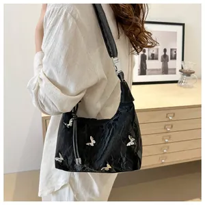 Detail of a crescent-shaped black shoulder bag with textured pleats and silver butterflies