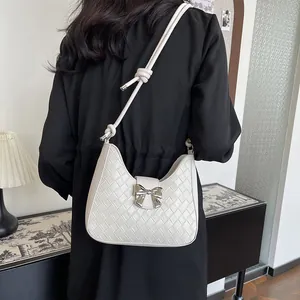 White woven shoulder bag with silver bow buckle worn by a model in a black dress