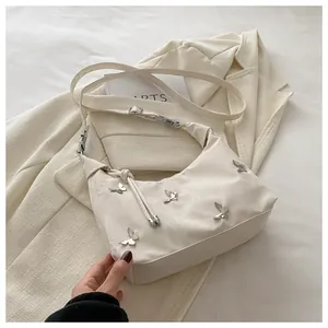 Close-up of cream nylon tote bag featuring silver butterfly hardware and adjustable strap