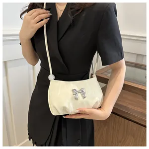Close-up of a white textured crossbody bag featuring a silver metal butterfly buckle detail