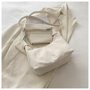 Close-up of cream crescent shoulder bag with silver hardware on beige blazer background