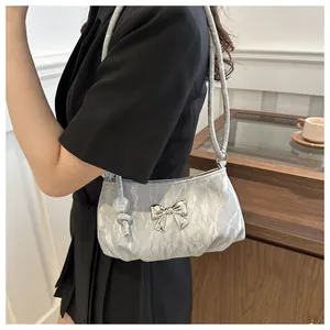 Detail of silver pleated shoulder bag featuring a metallic butterfly buckle on model