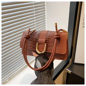 Détail du sac marron gaufré croco avec fermoir doré en U et bandoulière tressée à nœuds